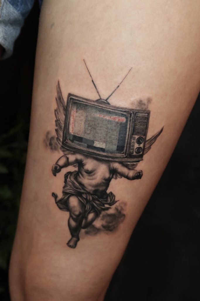 a tattoo of a baby angel with a tv head on it